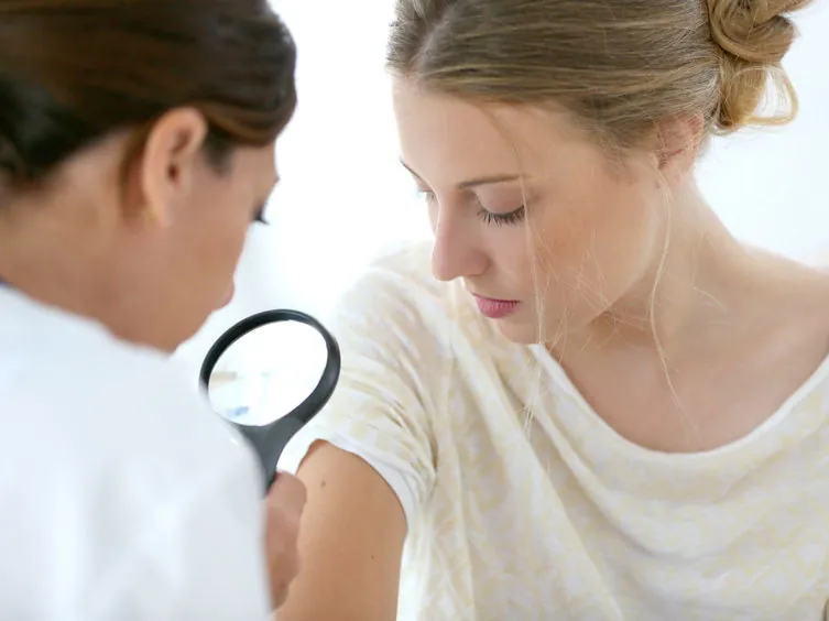 Médica examinando con lupa la piel del brazo de una paciente