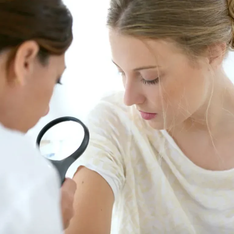 Médica examinando con lupa la piel del brazo de una paciente